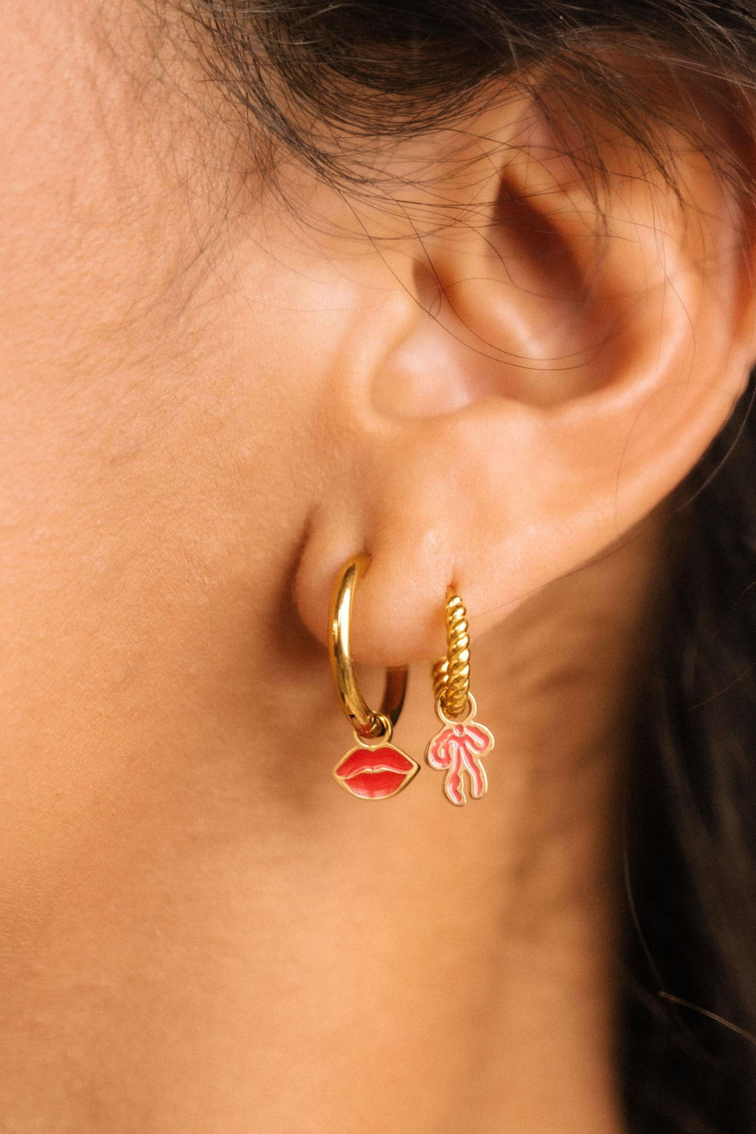 Close-up of an ear wearing gold hoop earrings with lip and flower charms.