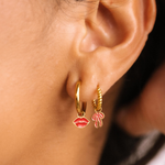 Close-up of an ear wearing gold hoop earrings with lip and bow charms.