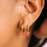 Close-up of an ear wearing gold hoop earrings with lip and bow charms.