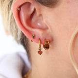 Close-up of a person wearing gold hoop earrings with heart-shaped charms.
