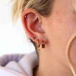 Close-up of a person wearing gold hoop earrings with a blurred background