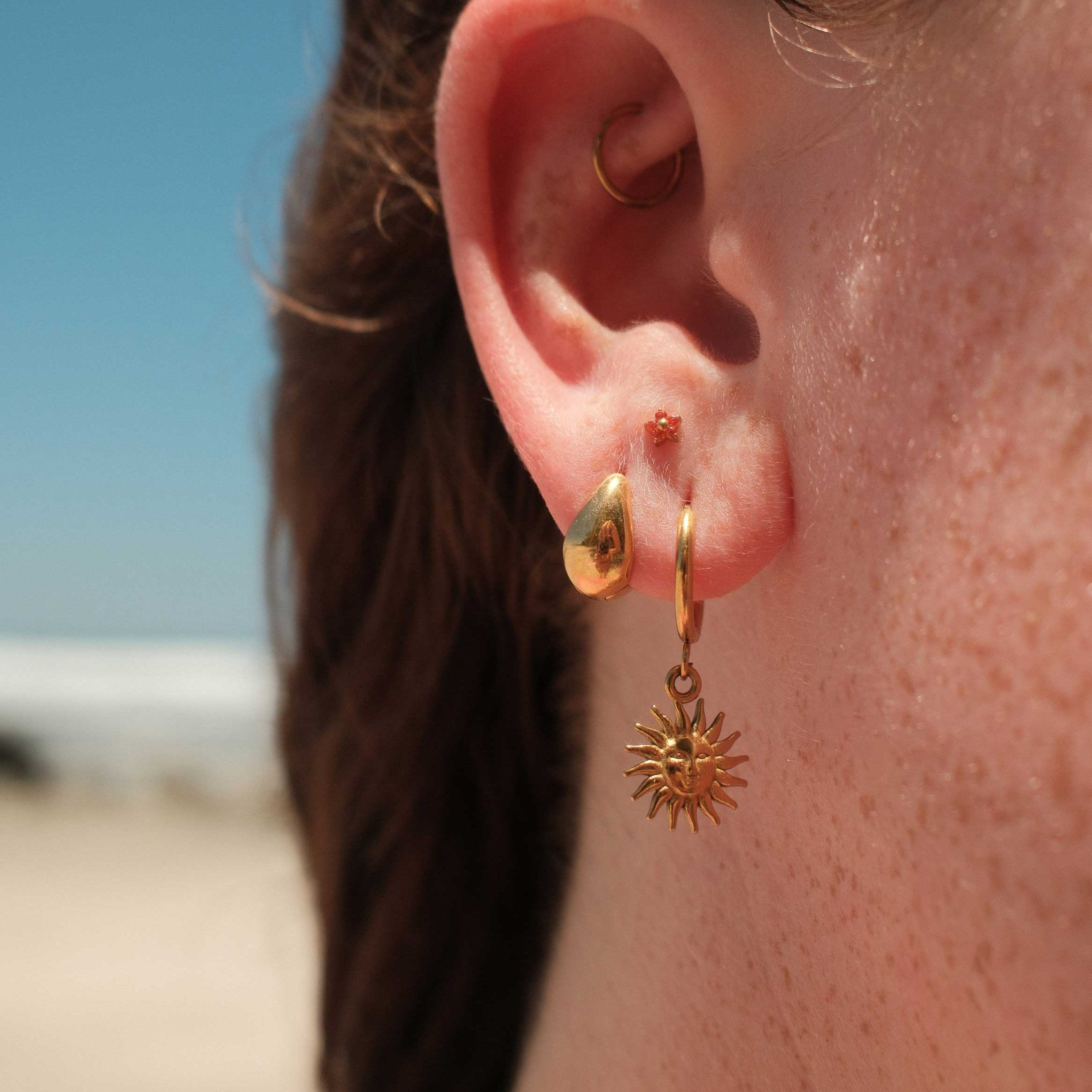Close-up of an ear with gold hoop earrings and an orange floral-shaped flat back stud.