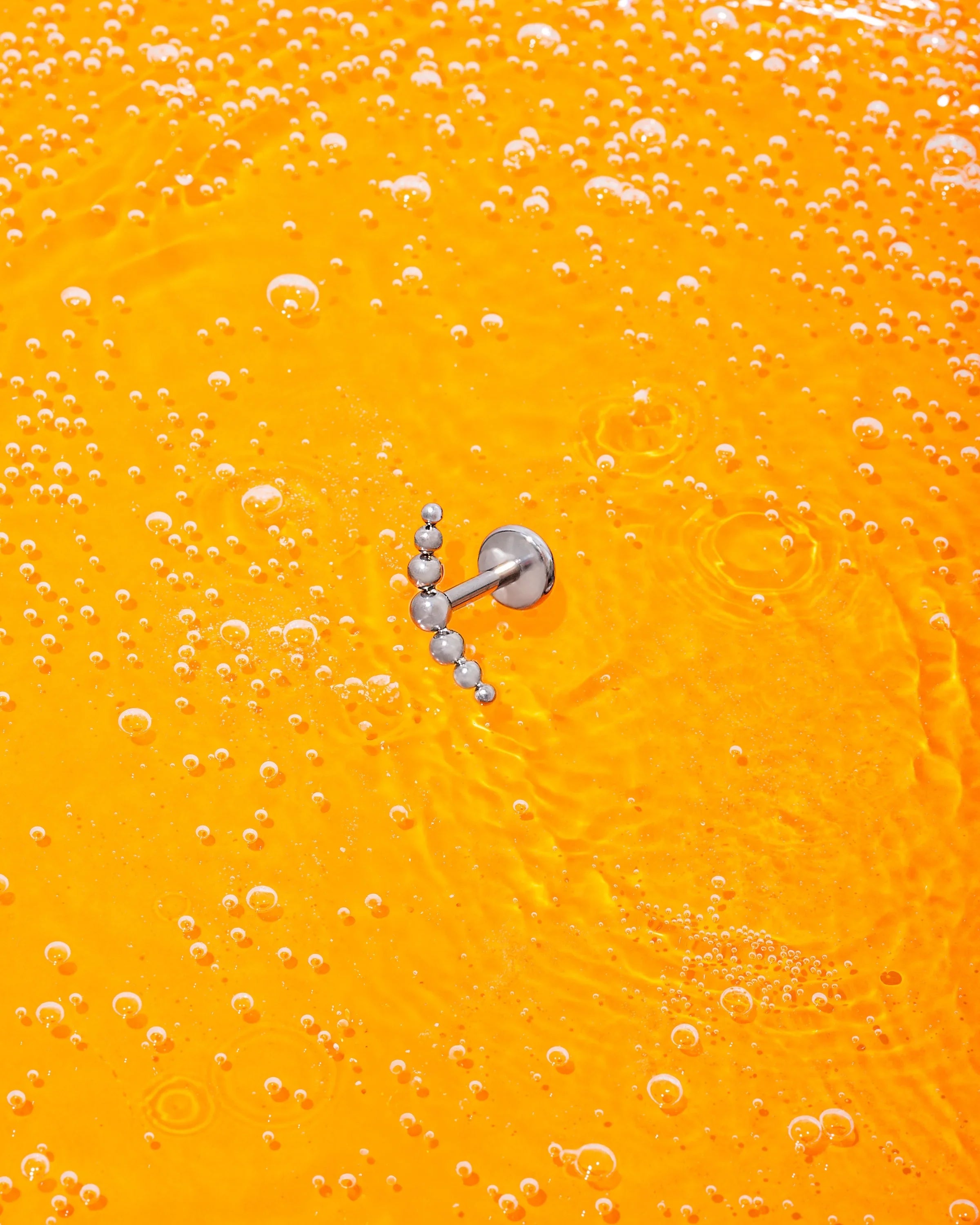 Silver earring on a bright orange background with bubbles
