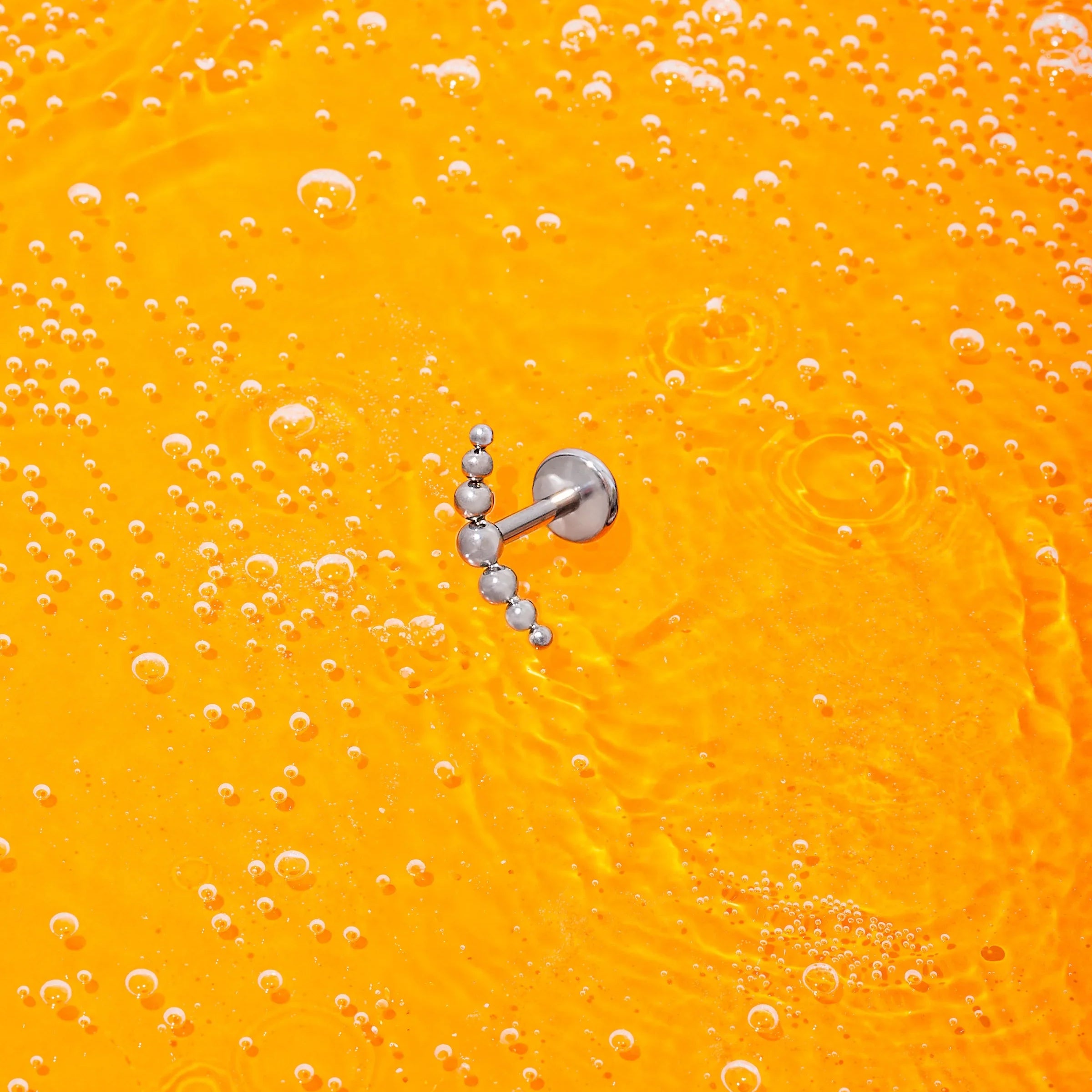 Silver earring on a bright orange background with bubbles