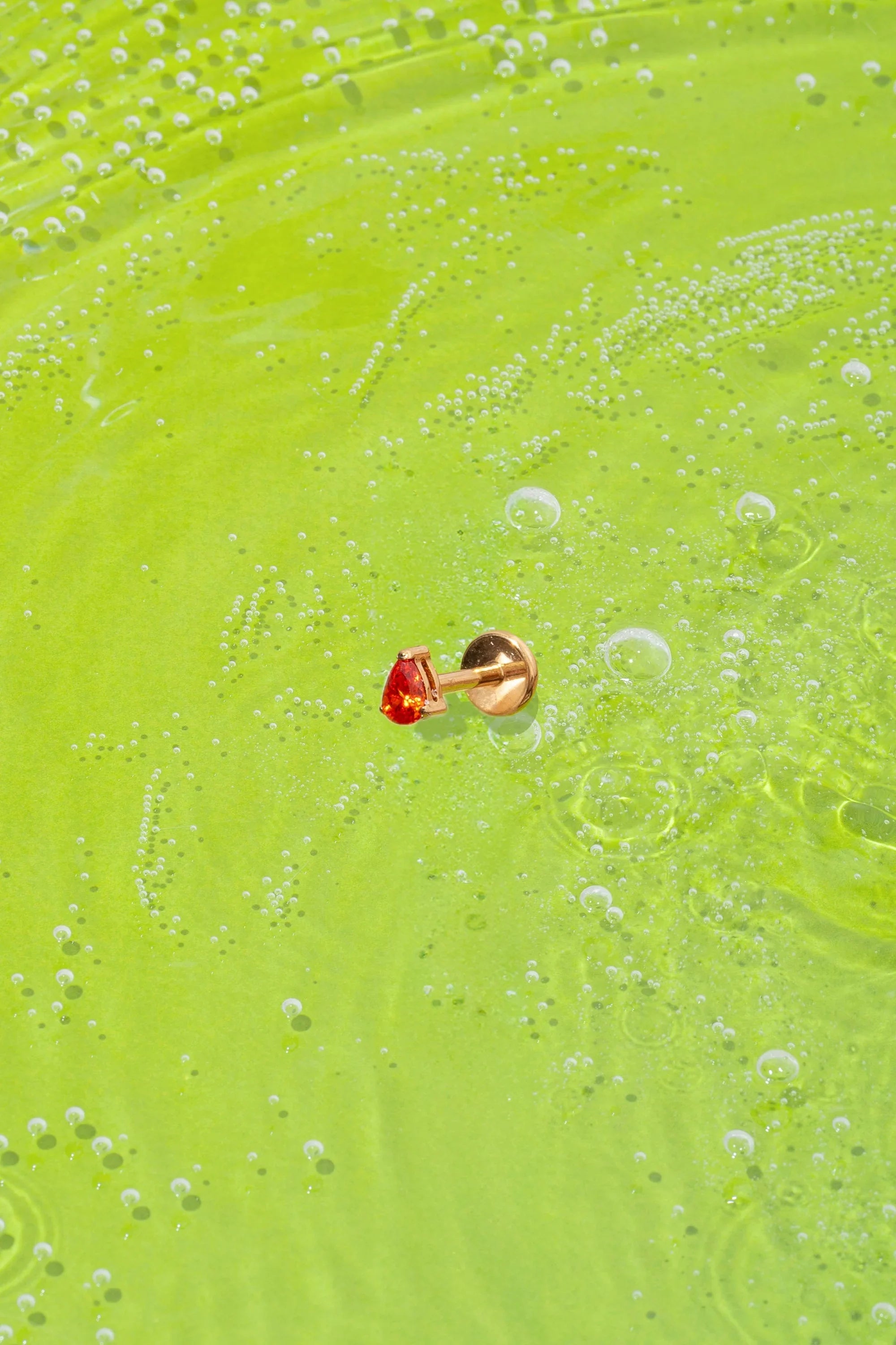 orange teardrop-shaped faceted gem flat back stud on a green textured surface with bubbles