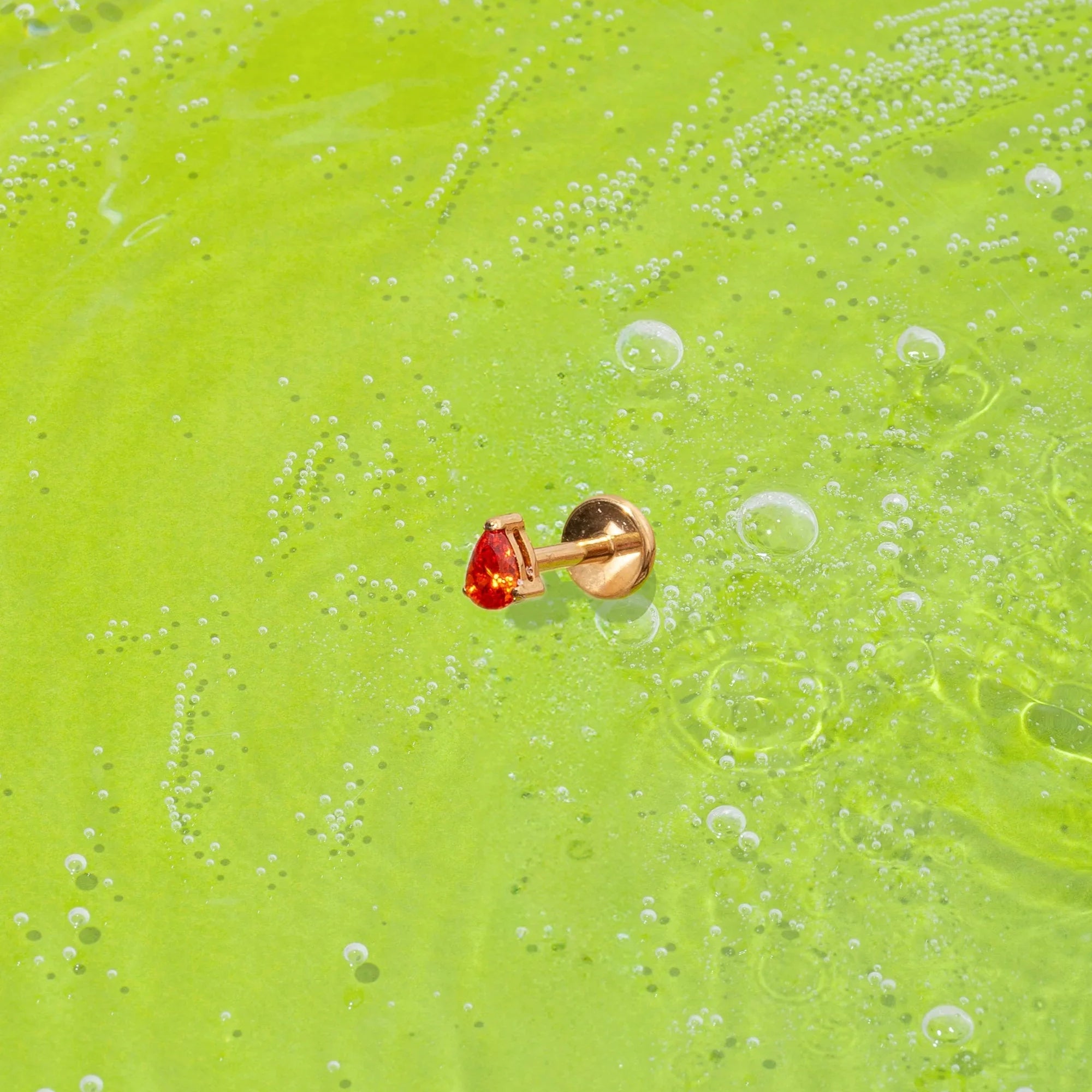 orange teardrop-shaped faceted gem flat back stud on a green textured surface with bubbles