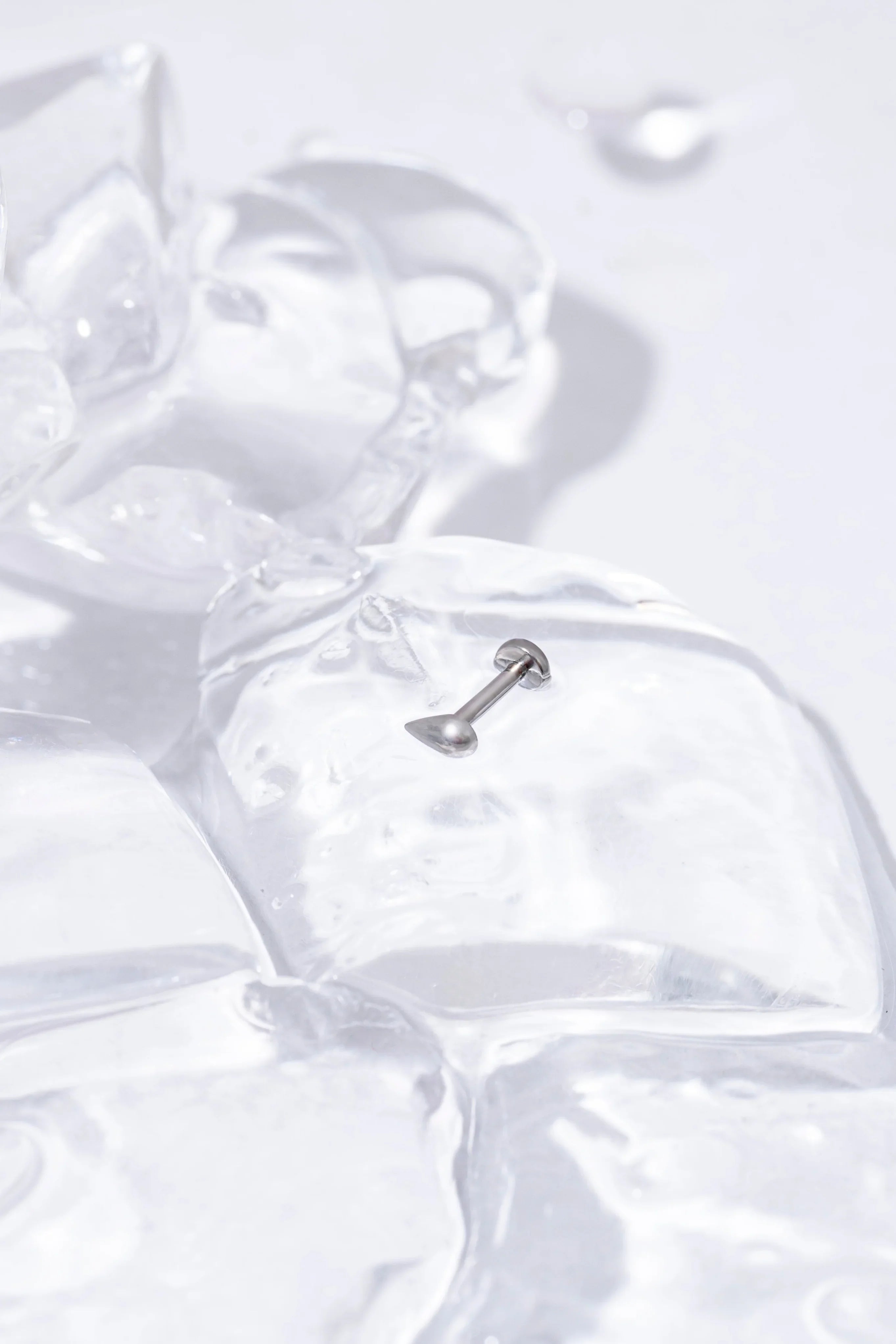Close-up of a silver 3D teardrop-shaped flat back stud on a background of ice cubes on a white surface.