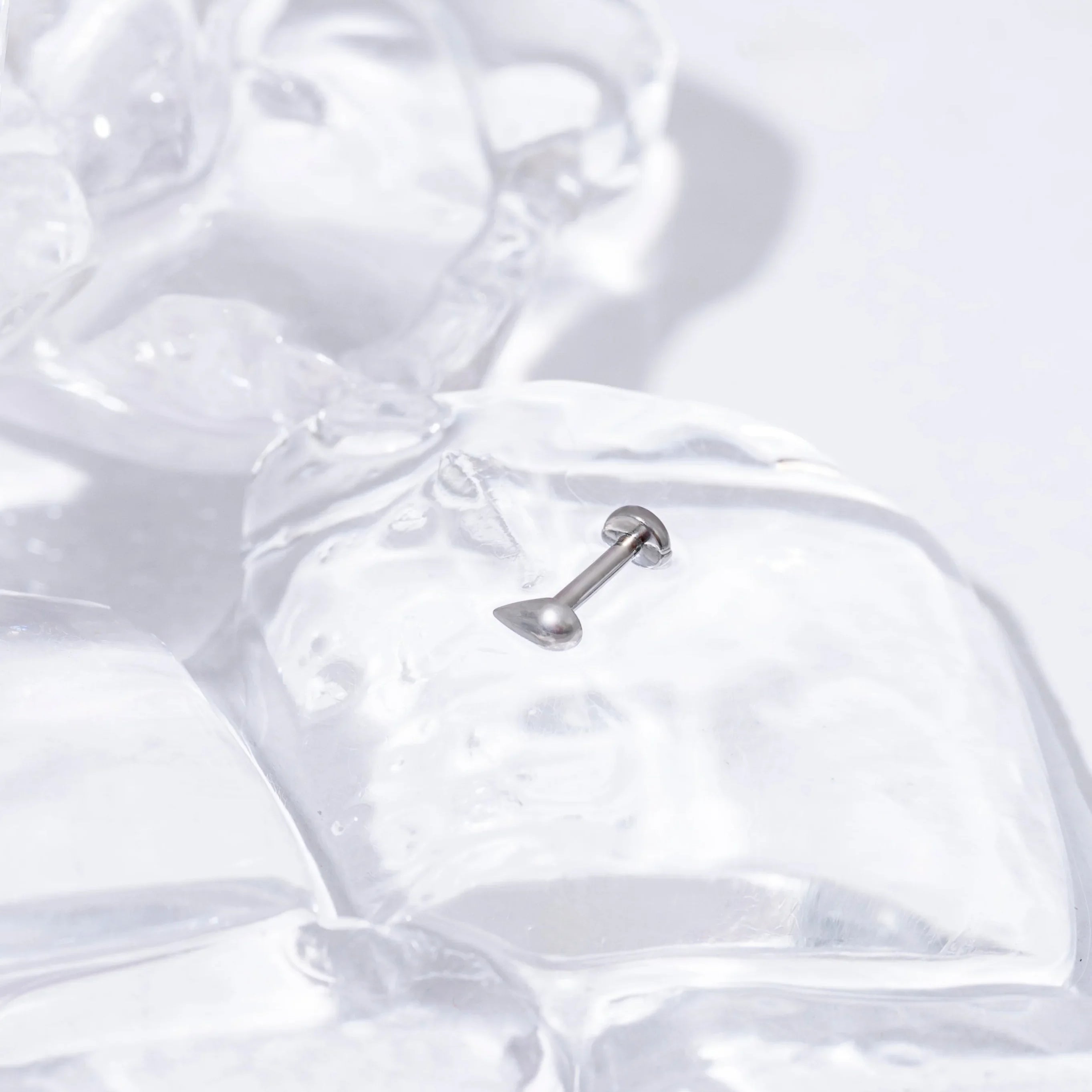 Close-up of a silver 3D teardrop-shaped flat back stud on a background of ice cubes on a white surface.