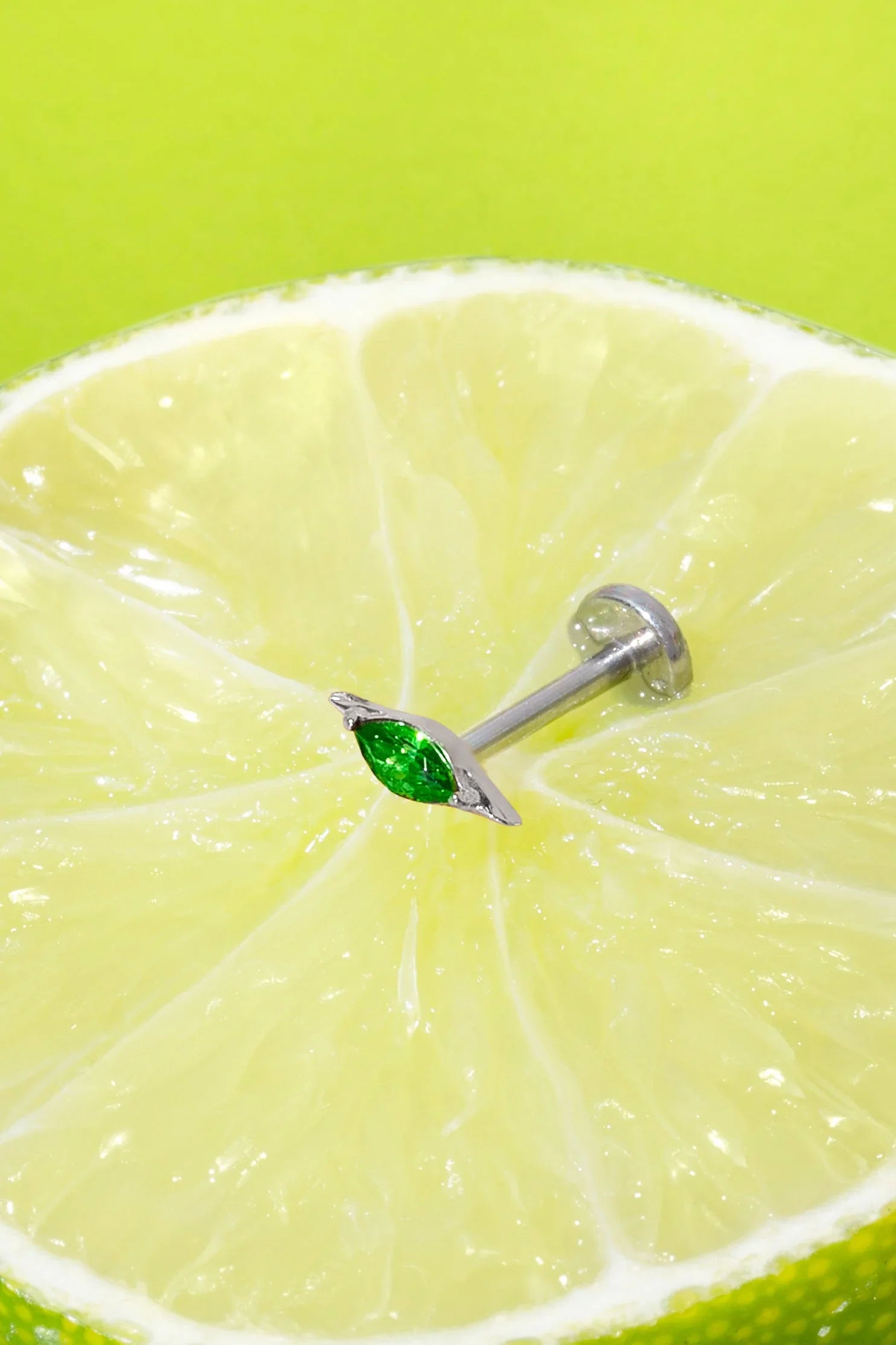 Lime wedge with a silver flat back stud earring featuring a green marquise gemstone on a green background