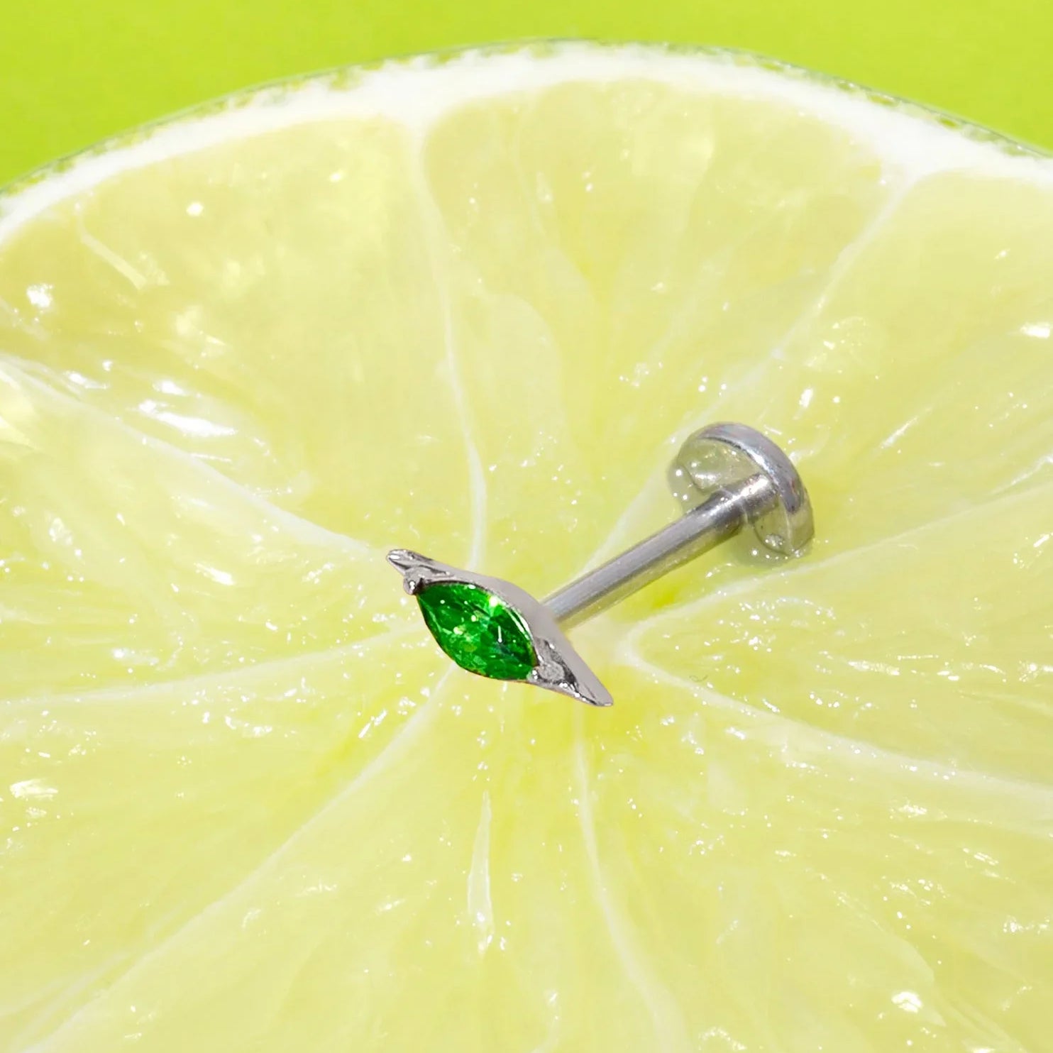 Lime wedge with a silver flat back stud earring featuring a green marquise gemstone on a green background