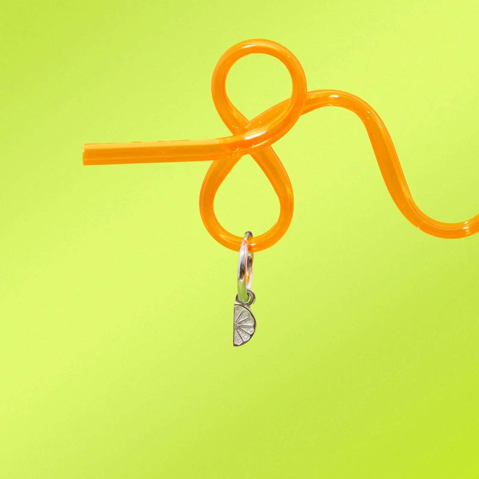 Orange straw with a silver 3D Lime wedge charm on a yellow-green background