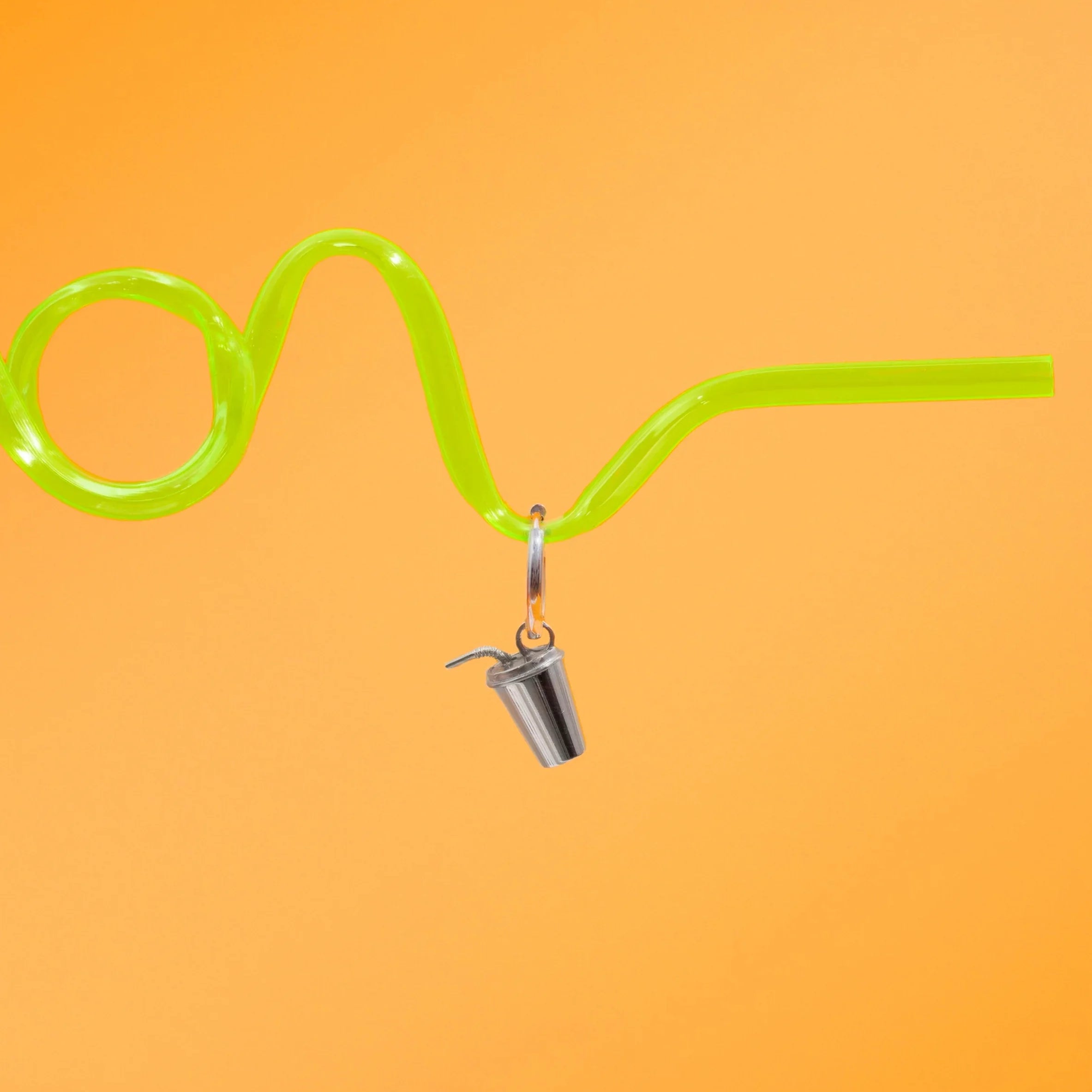 Green curly straw against a bright orange background, with a silver hoop with a silver metal, 3D fountain drink can charm.