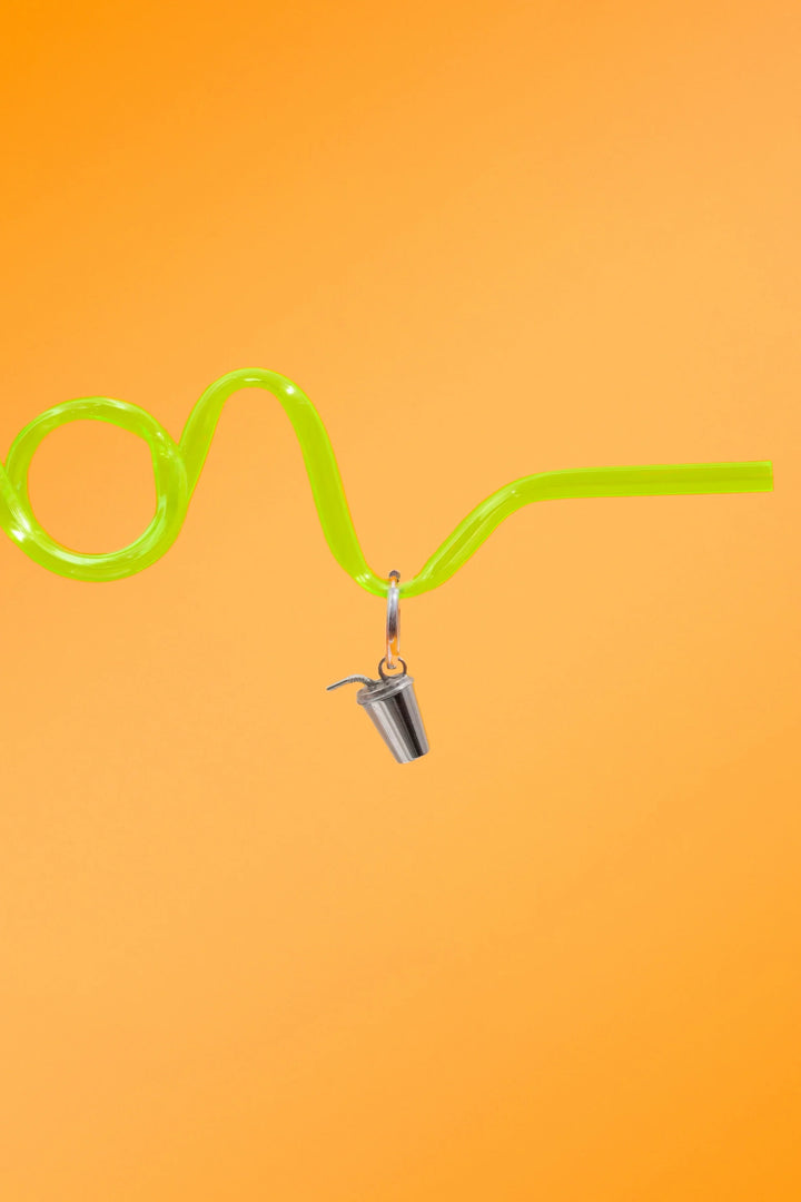 Green curly straw against a bright orange background, with a silver hoop with a silver metal, 3D fountain drink can charm.
