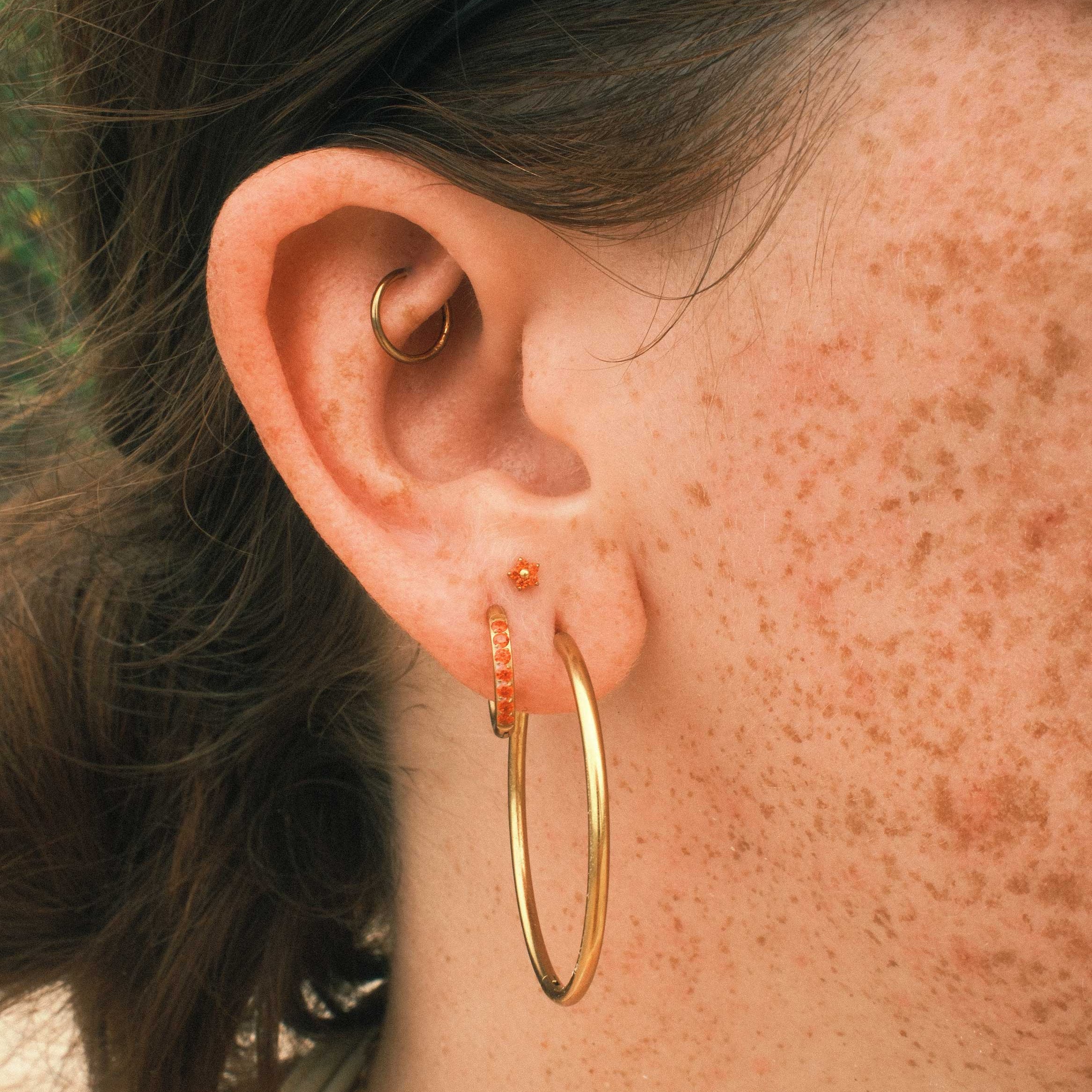 Close-up of an ear with gold hoop earrings and an orange floral-shaped flat back stud.