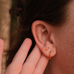 Close-up of an ear with two gold earrings, one being adjusted by a hand.