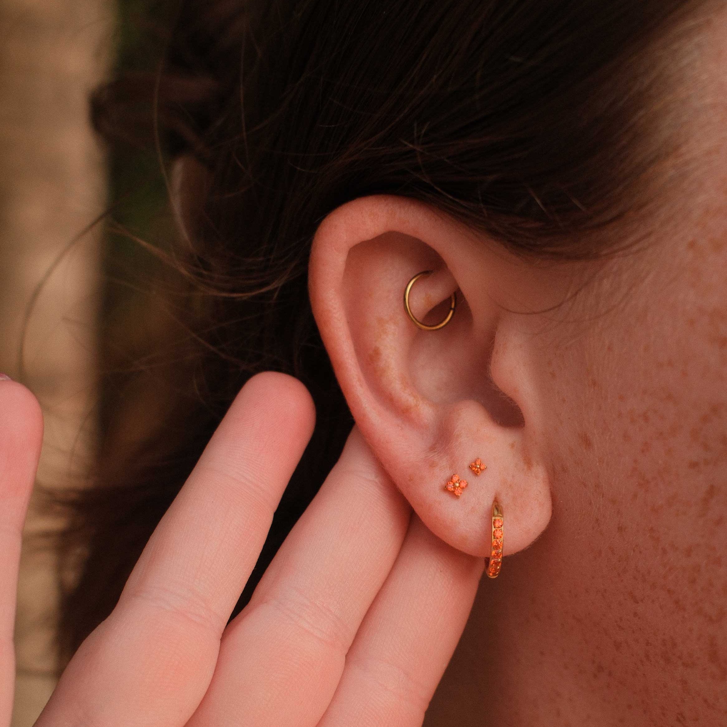 Close-up of an ear with two gold earrings, one being adjusted by a hand.