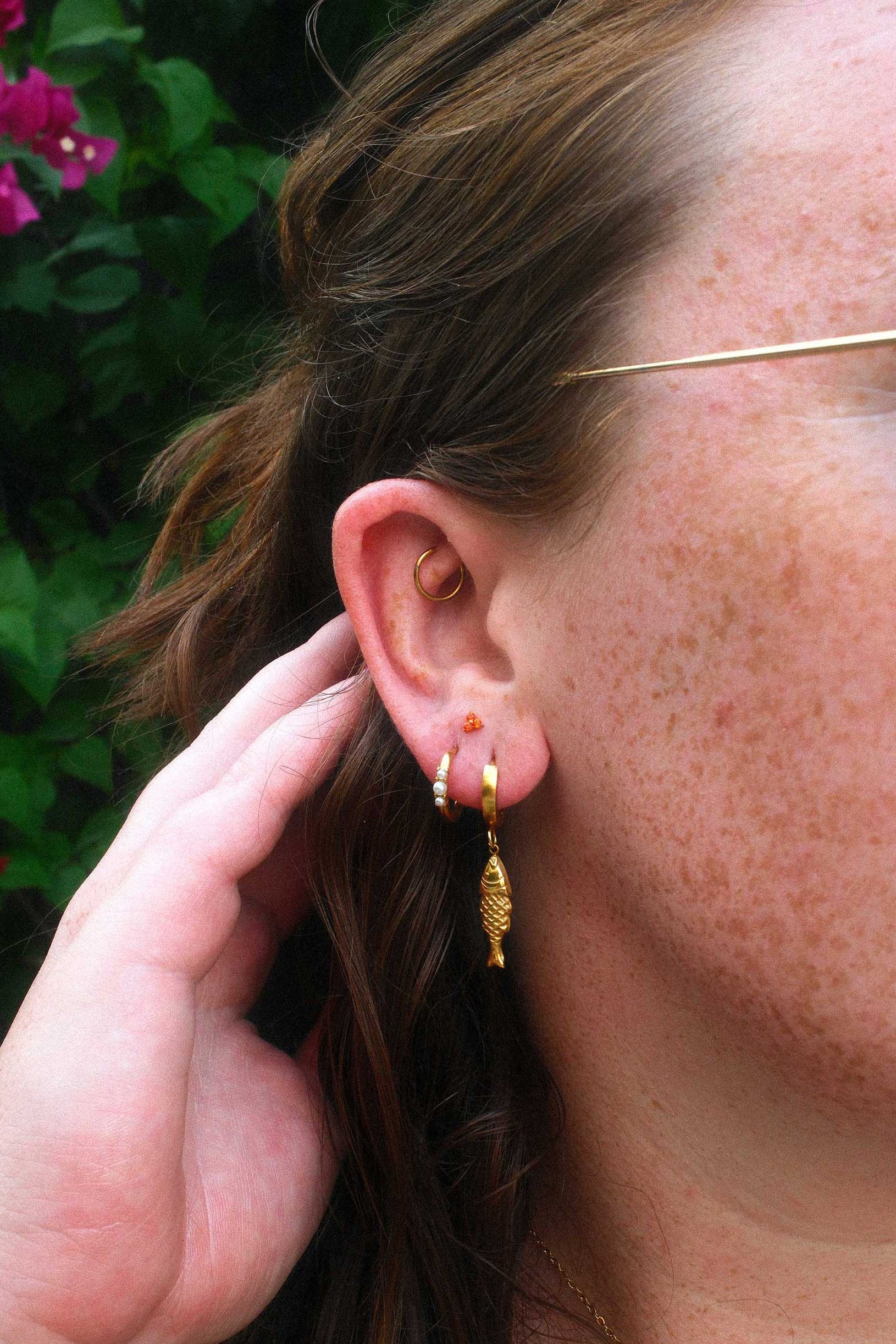 Close-up of a person wearing gold hoop earrings and an orange flat back stud with a blurred background