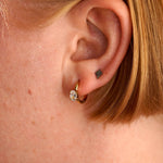 Close-up of an ear with a gold earring and black tattoo on the lobe.