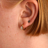 Close-up of an ear with a gold earring and black tattoo on the lobe.