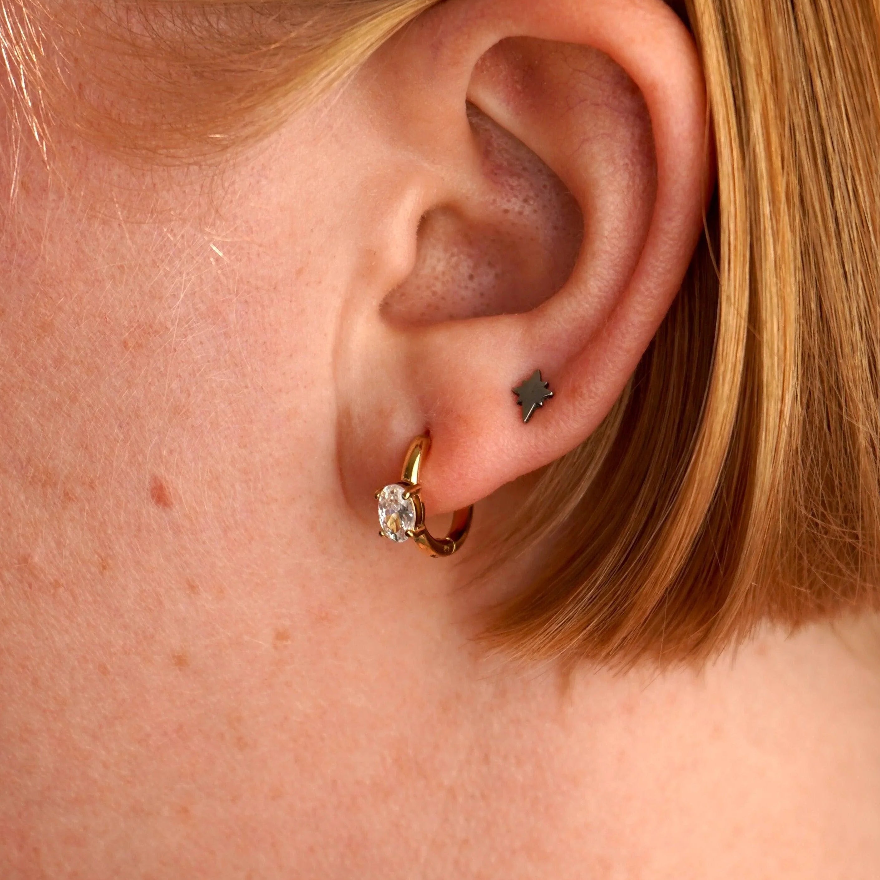 Close-up of an ear with a gold earring and black tattoo on the lobe.