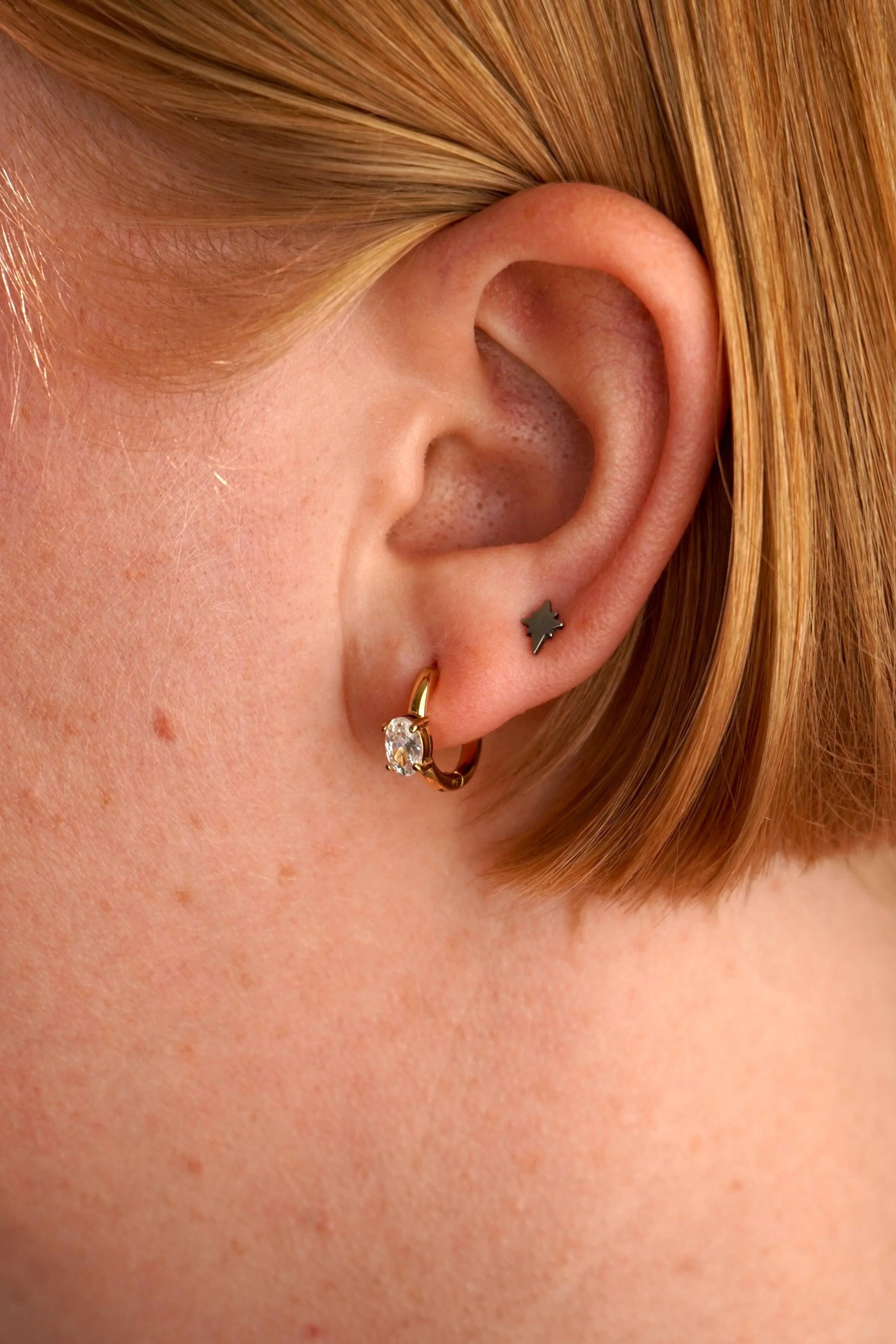 Close-up of an ear with a gold earring and black tattoo on the lobe.