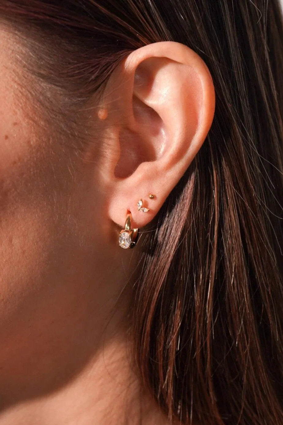 Close-up of an ear with gold earrings against a blurred background