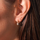 Close-up of an ear with gold earrings against a blurred background