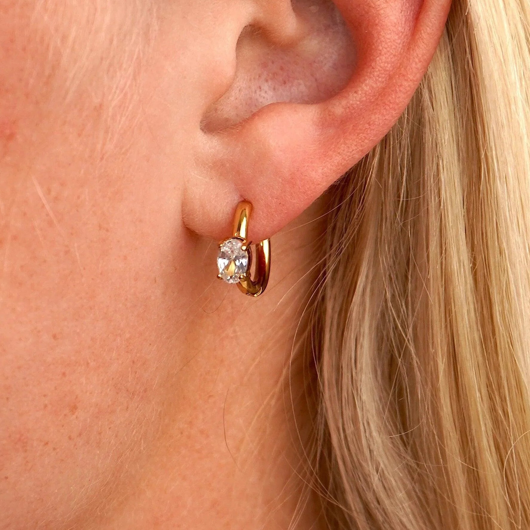 Close-up of a person wearing a gold hoop earring with a clear gemstone.