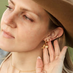 Woman wearing a brown hat and gold jewelry, including earrings and a necklace.
