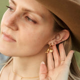 Woman wearing a brown hat and gold jewelry, including earrings and a necklace.
