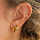 Close-up of a person wearing gold earrings with a blurred background