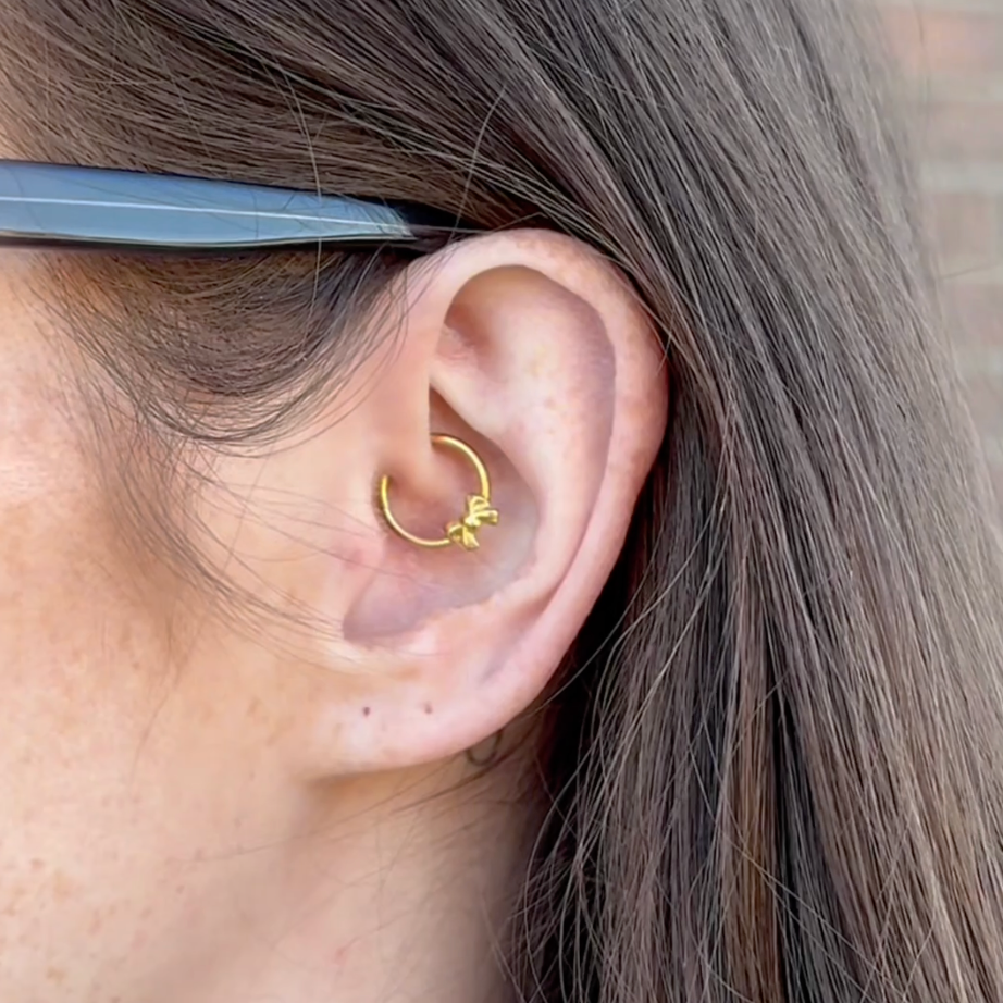 Close-up of an ear with a gold bow daith hoop earring, hair partially covering the face.