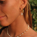 Close-up of a woman wearing gold hoop earrings and pearl necklaces with a blurred green background
