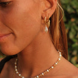 Close-up of a woman wearing gold hoop earrings and pearl necklaces with a blurred green background