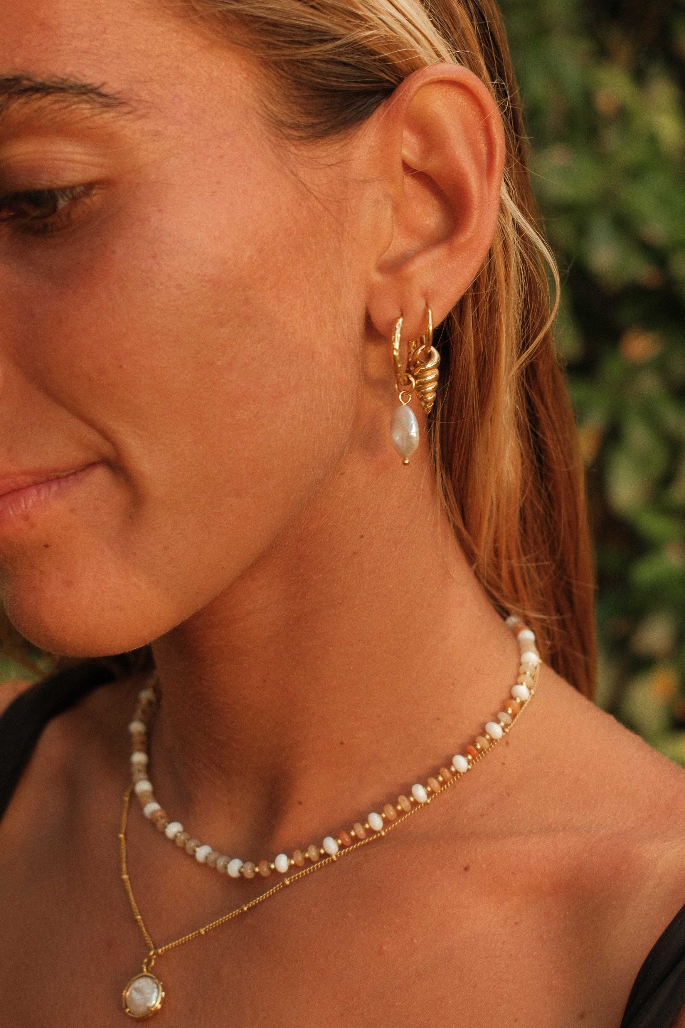 Close-up of a woman wearing gold hoop earrings and pearl necklaces with a blurred green background