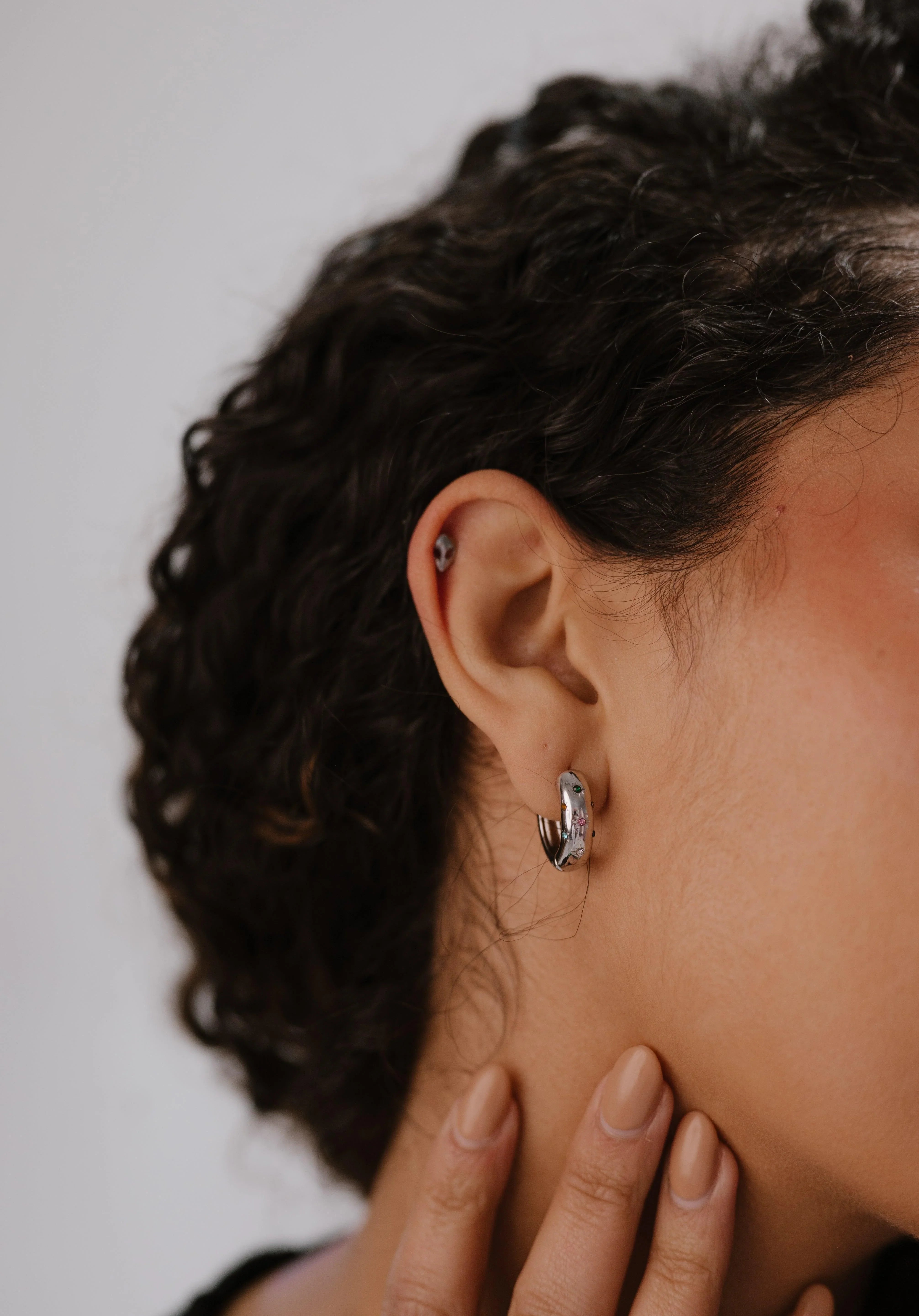 Close-up of an ear with a hoop earring against a neutral background
