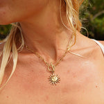 Close-up of a person wearing a gold necklace with a sun pendant.