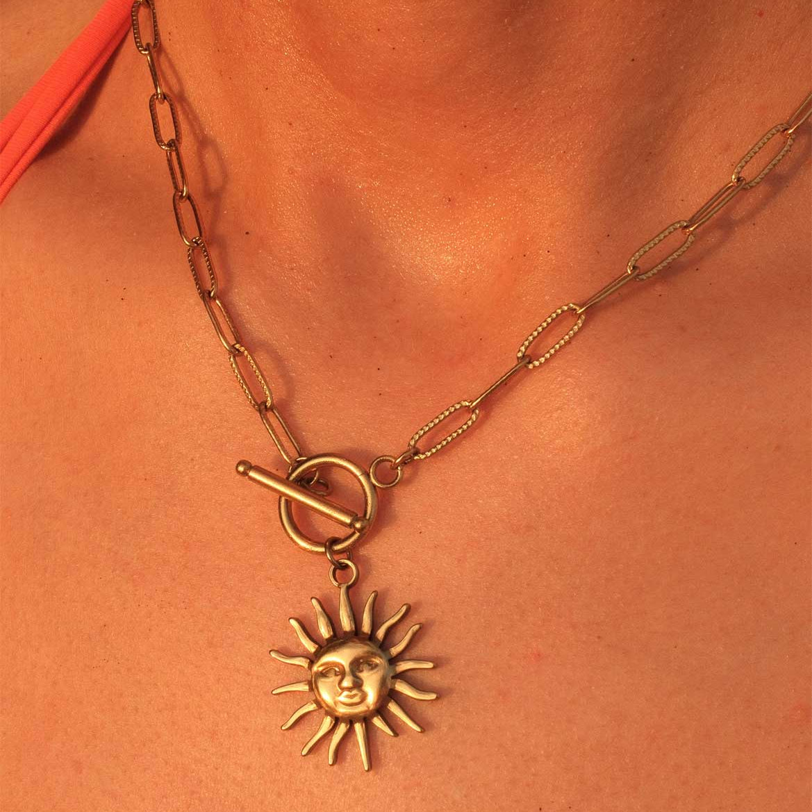 Gold necklace with a sun pendant on a person's neck