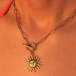 Gold necklace with a sun pendant on a person's neck