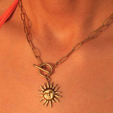 Gold necklace with a sun pendant on a person's neck