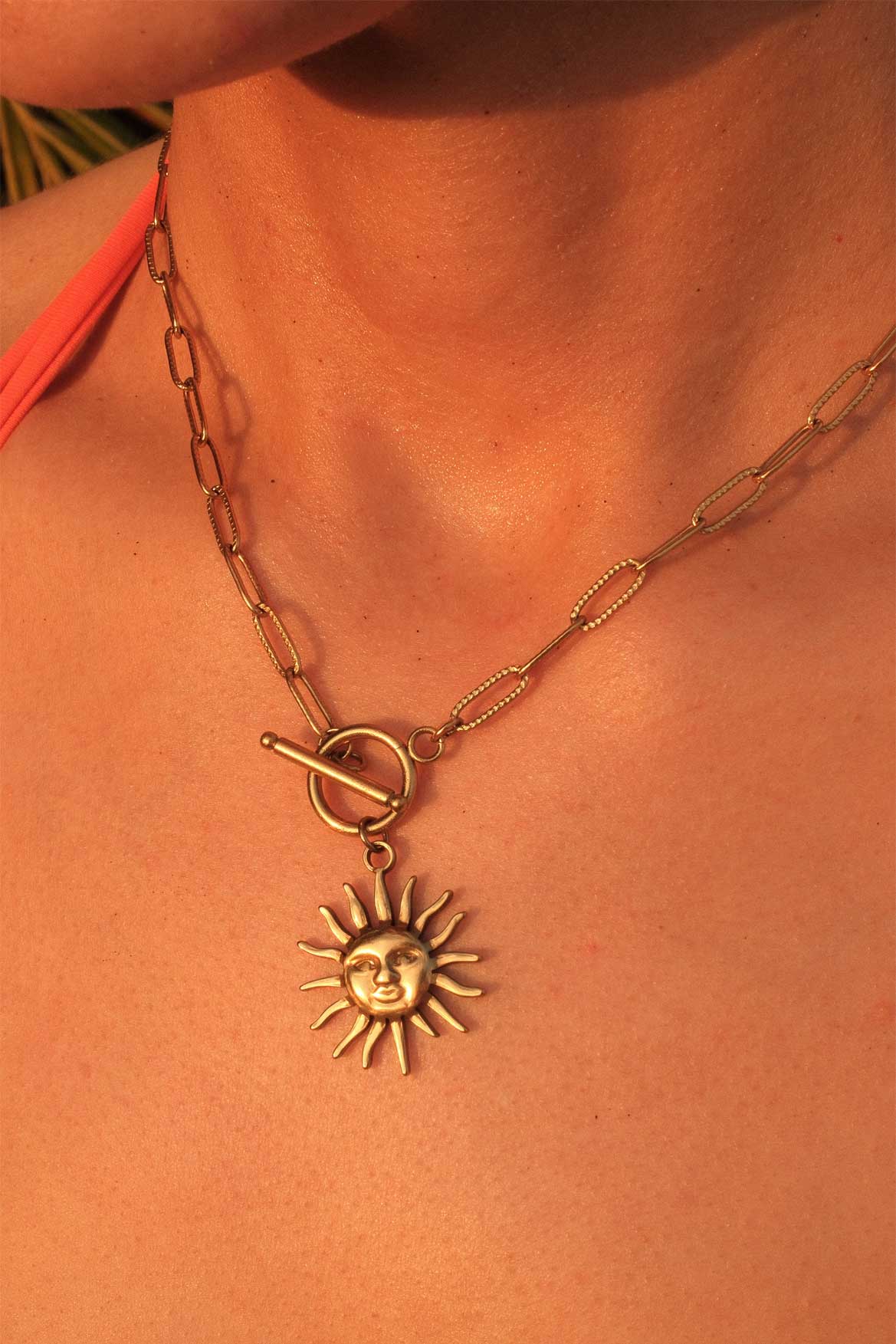 Gold necklace with a sun pendant on a person's neck