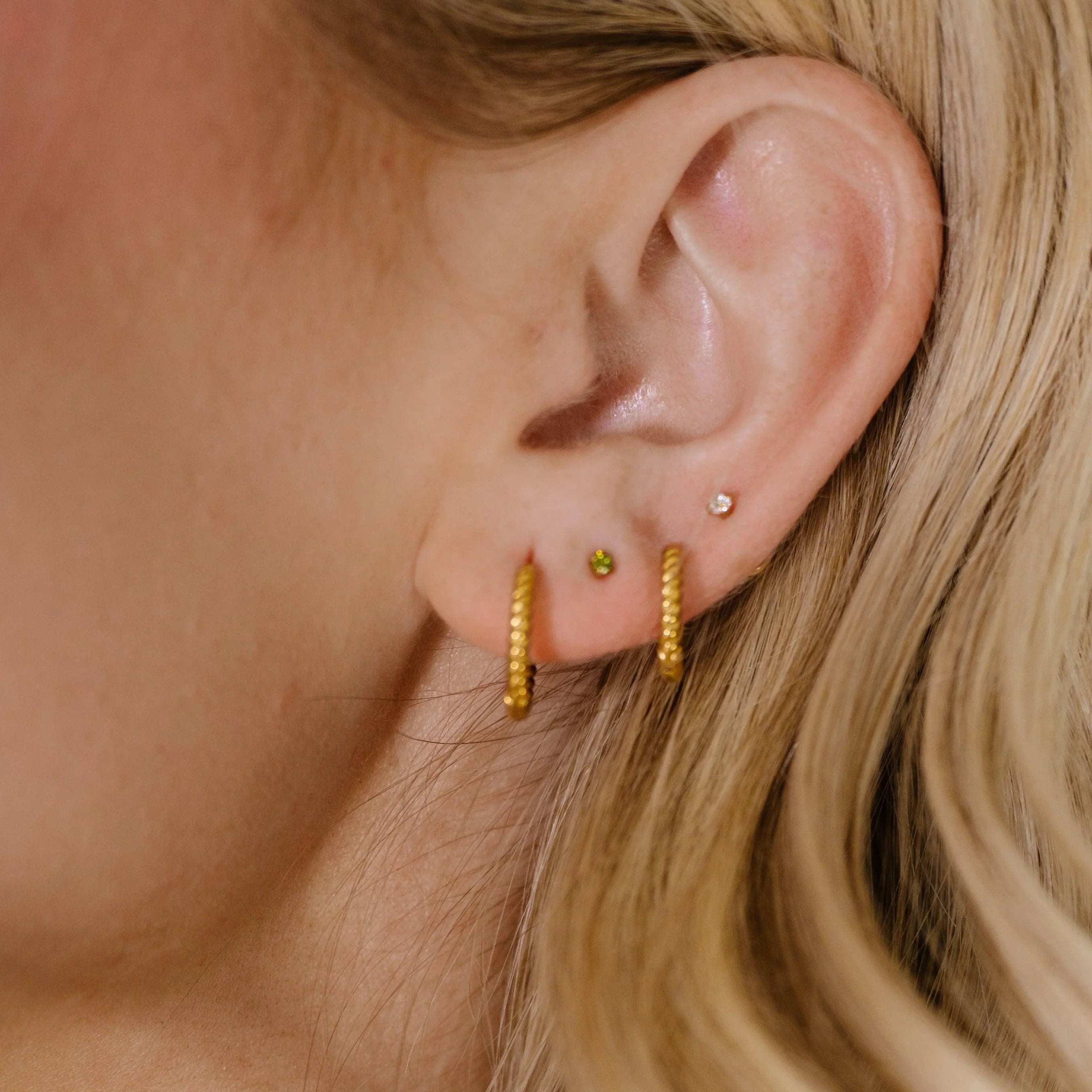 Close-up of a person with blonde hair, wearing two gold hoop earrings and two CZ stud earrings.