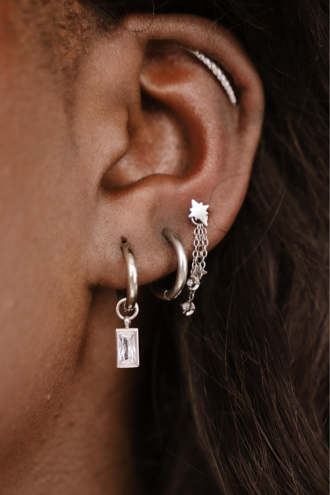 Close-up of an ear with multiple silver hoop earrings.