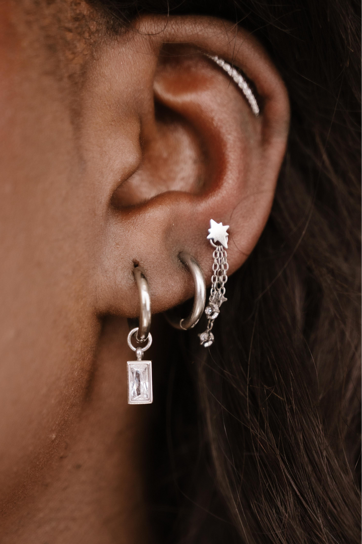 Close-up of an ear with multiple silver hoop earrings.