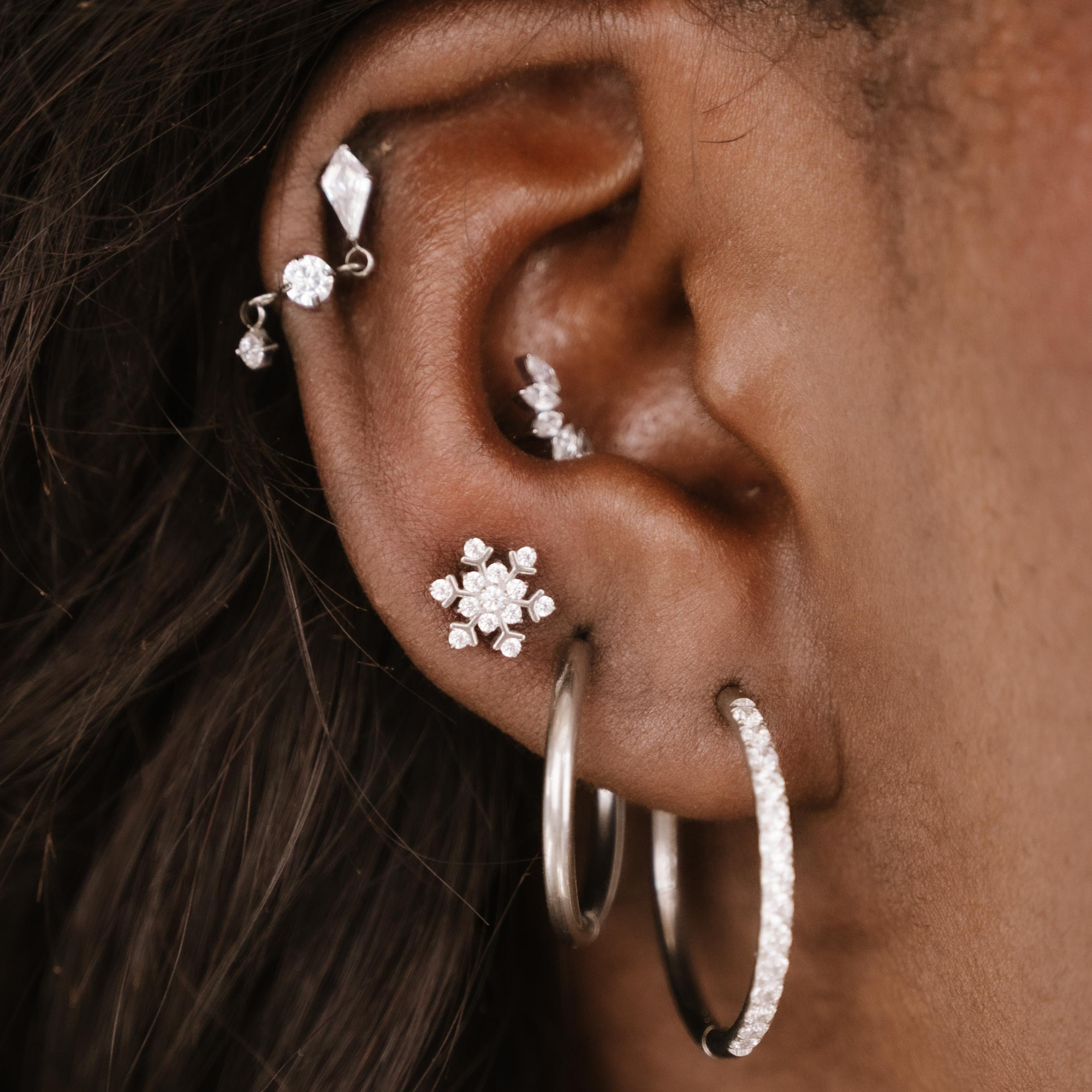 Close-up of an ear with multiple silver and clear zirconia earrings