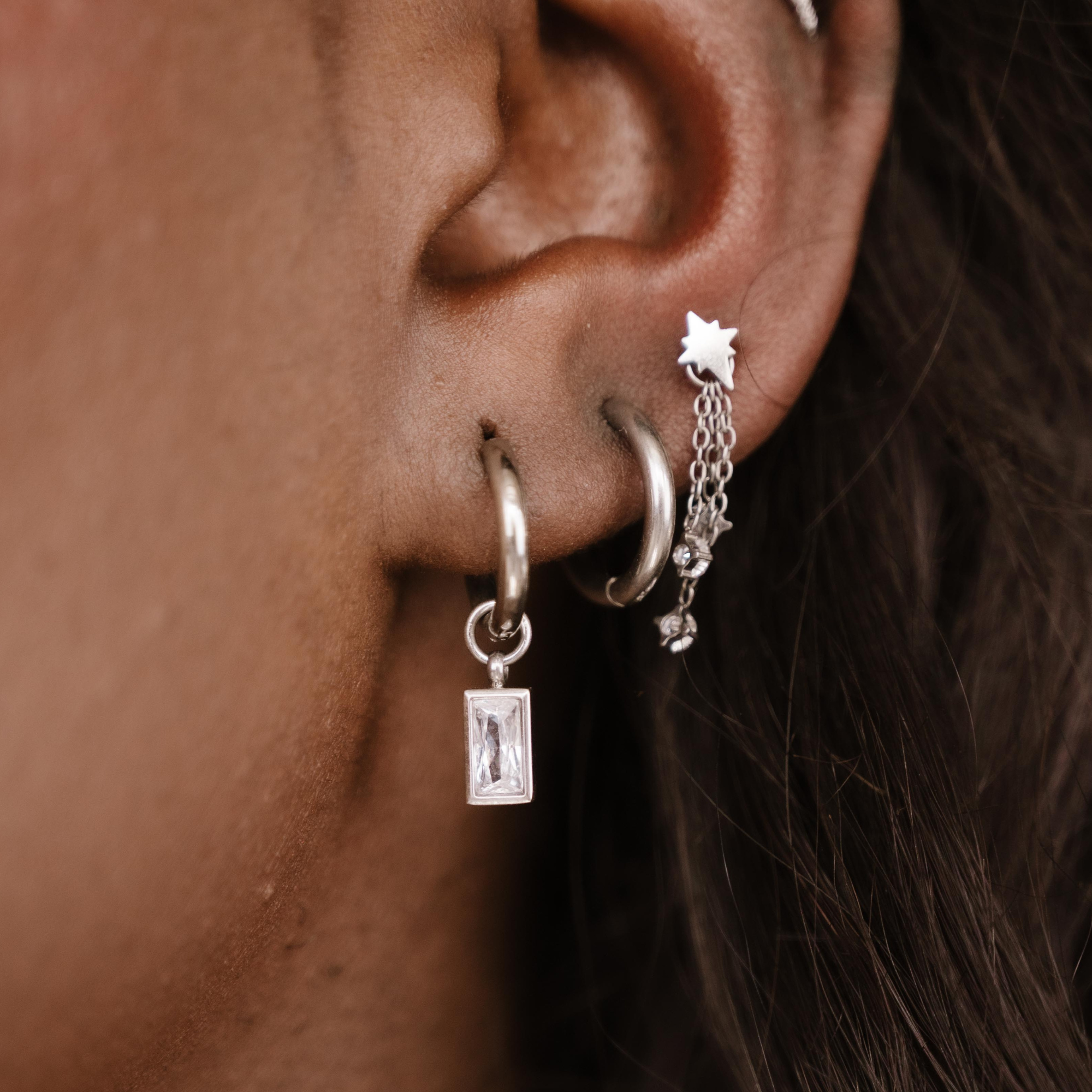 Close-up of an ear with multiple silver hoop earrings.