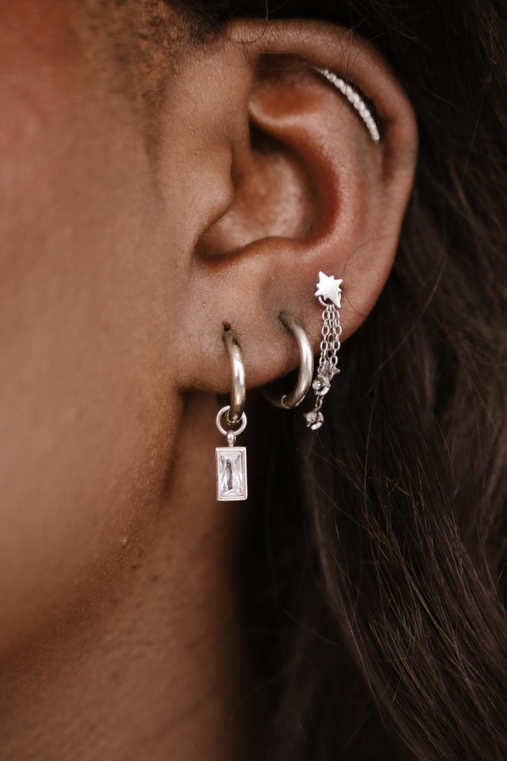 Close-up of an ear with multiple silver hoop earrings.