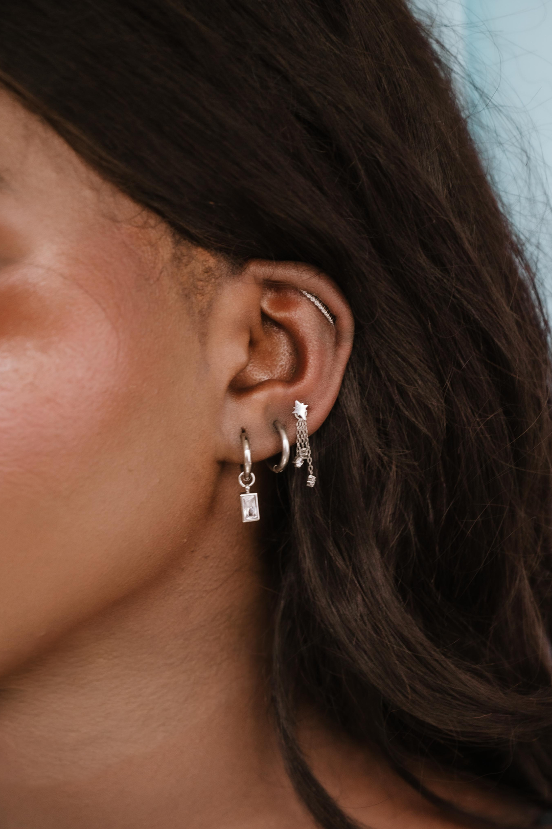 Close-up of an ear with multiple earrings against a blurred background