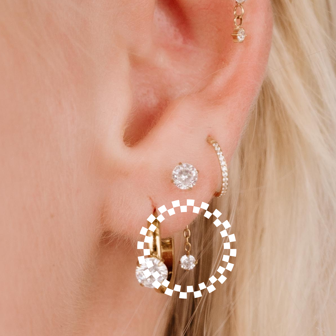 Close-up of an ear wearing gold hoop earrings with clear gemstones.