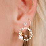 Close-up of an ear wearing gold hoop earrings with clear gemstones.